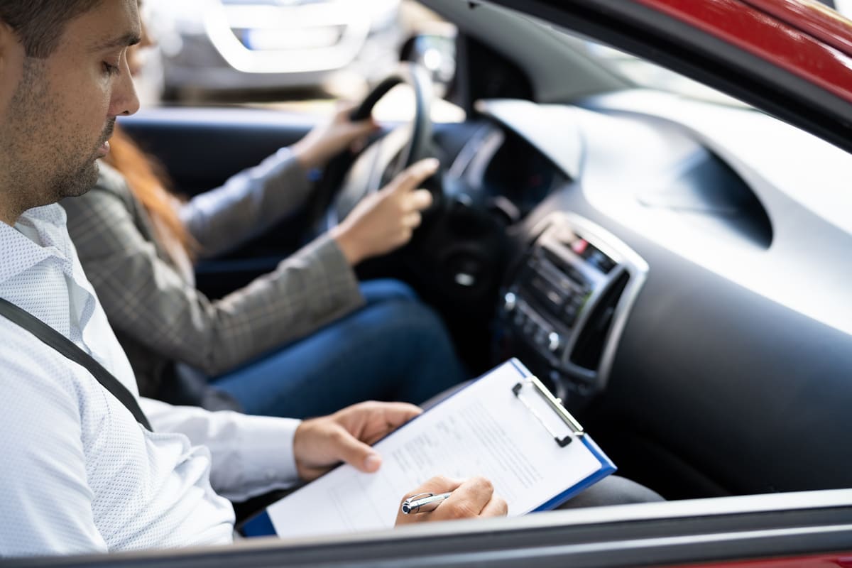 femme passant un examen de conduite dans une voiture avec un examinateur  qui prend des notes dans son cahier 